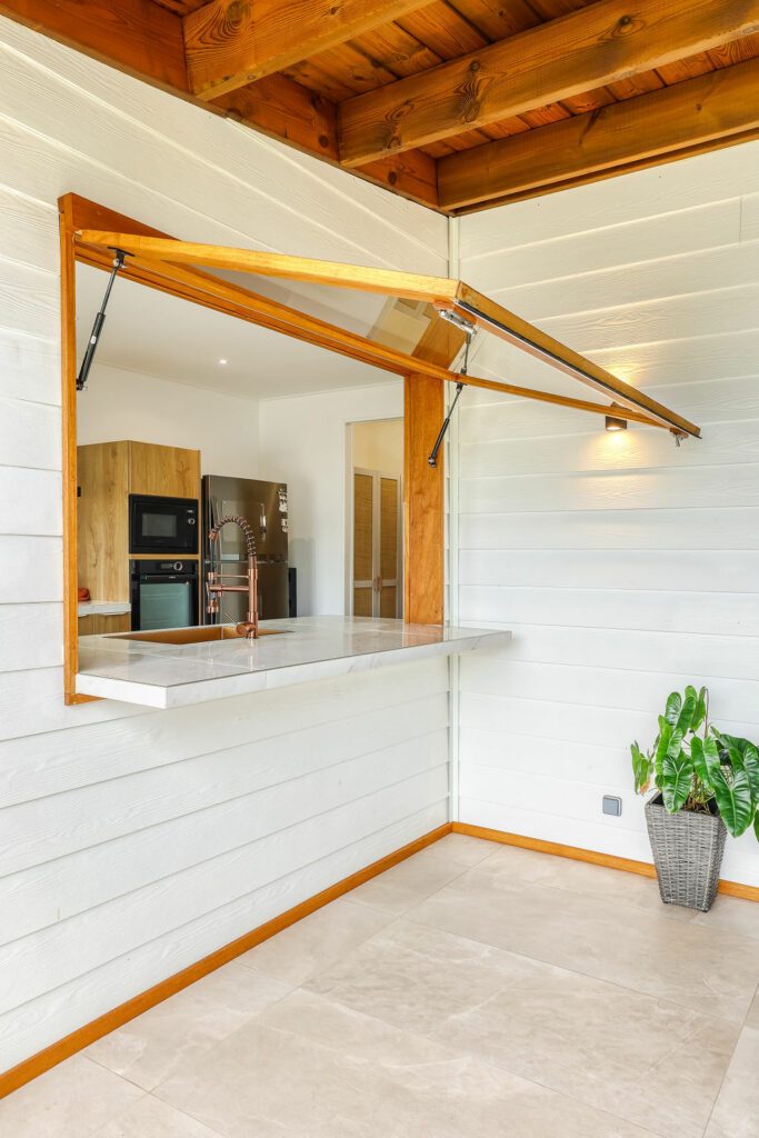 Fenêtre à l'italienne de la cuisine donnant sur la terrasse d'une maison en bois/béton